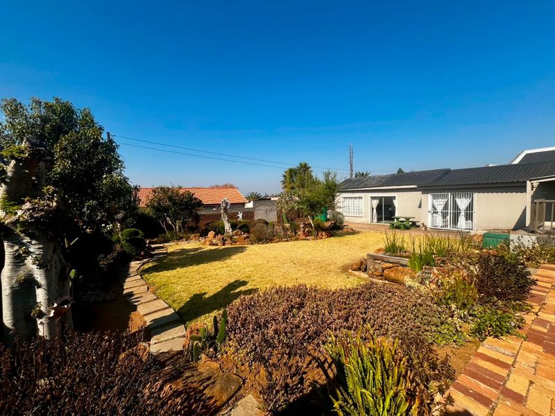 A well-maintained rear garden featuring a lawn, stone pathways, and established landscaping, providing access to the main dwelling via sliding glass doors.