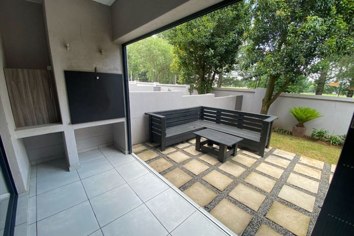 A covered patio featuring a built-in braai, tiled flooring, and a seamless transition to a paved outdoor garden area with boundary walls.