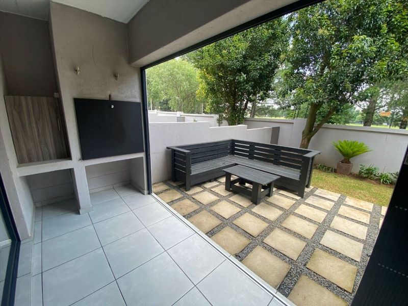 A covered patio featuring a built-in braai, tiled flooring, and a seamless transition to a paved outdoor garden area with boundary walls.