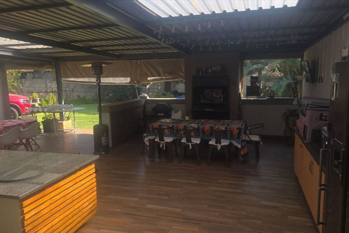 Spacious covered outdoor patio featuring timber-look flooring, built-in cabinetry with stone countertops, and a built-in braai area, perfect for alfresco dining.