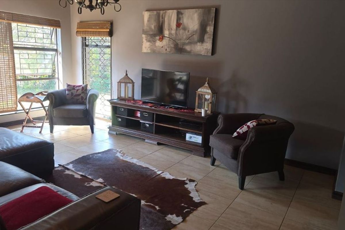 A comfortable living room featuring tiled flooring and large windows fitted with security bars, providing natural light and a view of the exterior.