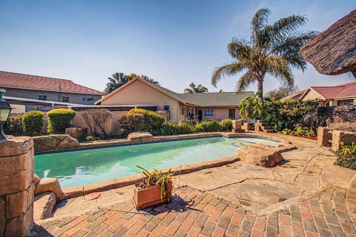 A backyard pool area featuring a rock-edged swimming pool, paved patio space, and established garden landscaping.