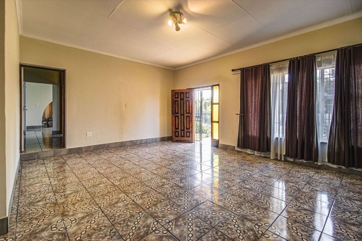 Spacious, empty living room featuring patterned ceramic floor tiles, neutral walls, and direct access to an outdoor area through a timber door.