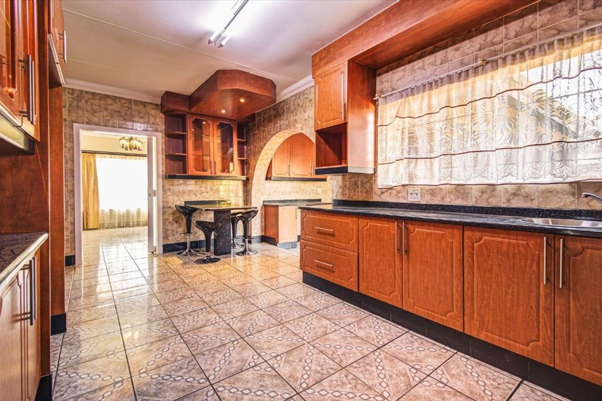 A spacious kitchen featuring extensive wooden cabinetry, granite countertops, tiled flooring, and a distinctive architectural archway leading to an adjacent room.
