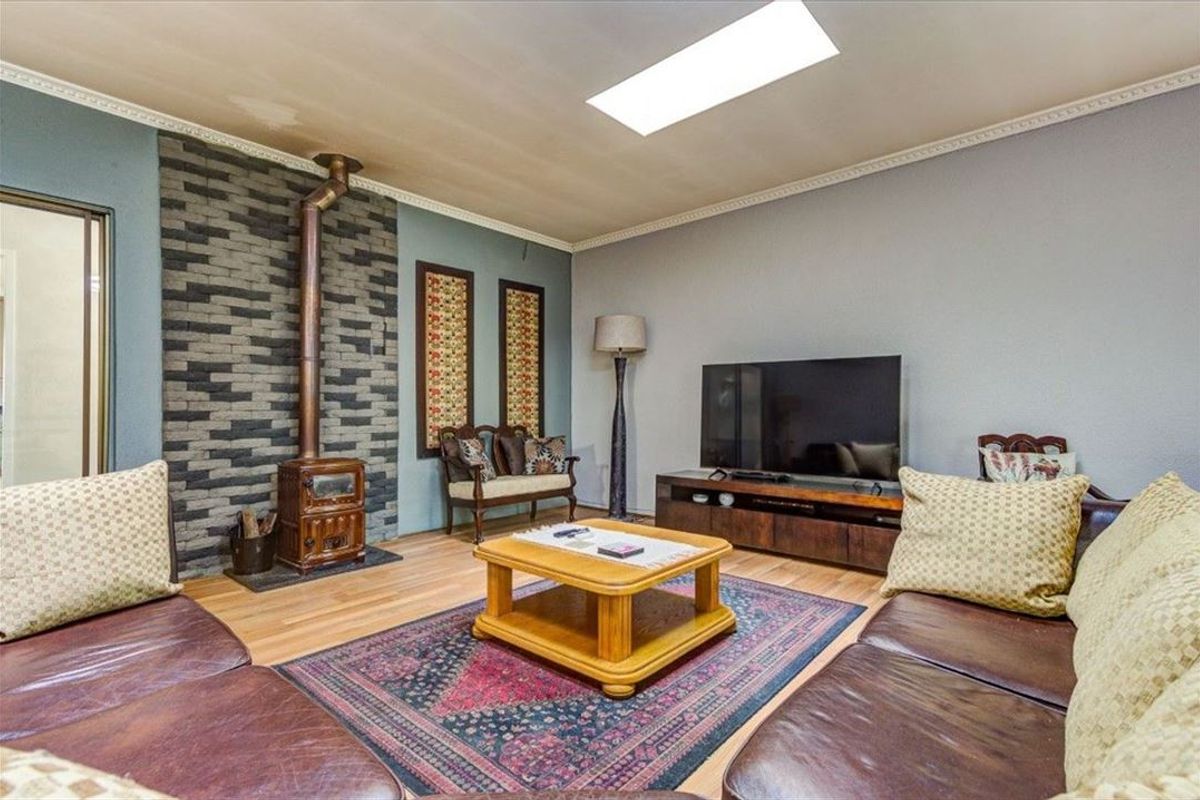 A cozy living room featuring a stone accent wall with a wood-burning stove, hardwood flooring, and a skylight providing natural light.