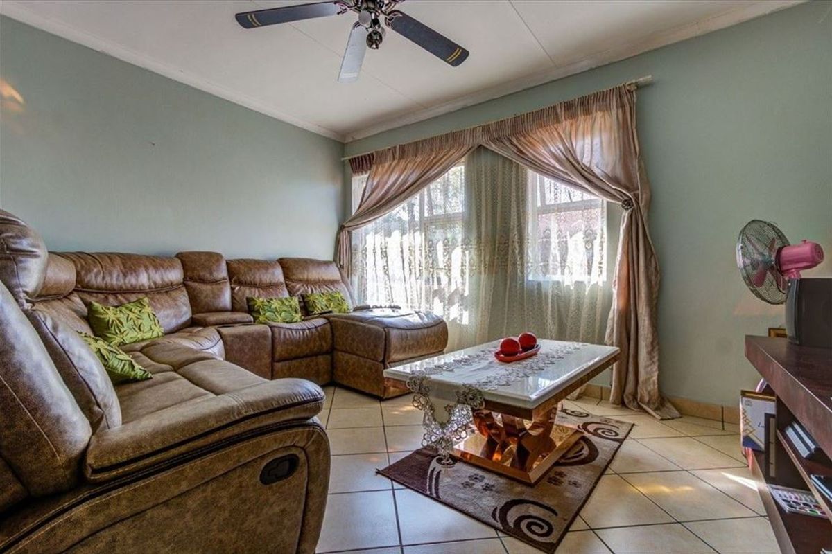A comfortable living room featuring tiled flooring, a ceiling fan, and natural light through large windows.