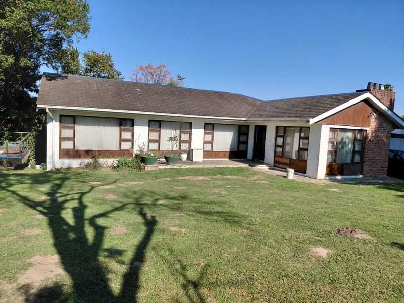 Rear view of a single-story brick house featuring a large lawn, concrete patio area, and traditional timber-framed windows.
