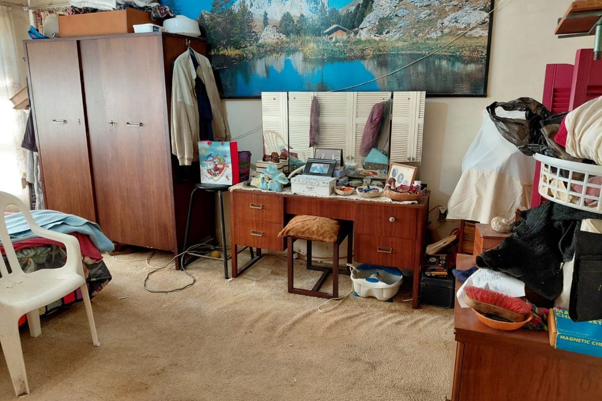 A bedroom featuring carpet flooring, currently cluttered with personal belongings and furniture.
