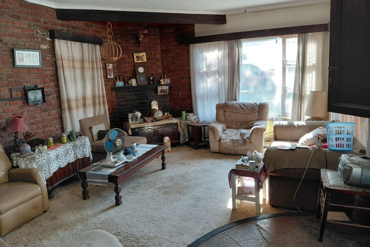 A living room featuring exposed brick walls, a brick fireplace, timber ceiling beams, and stone flooring, offering a rustic aesthetic with potential for modernization.
