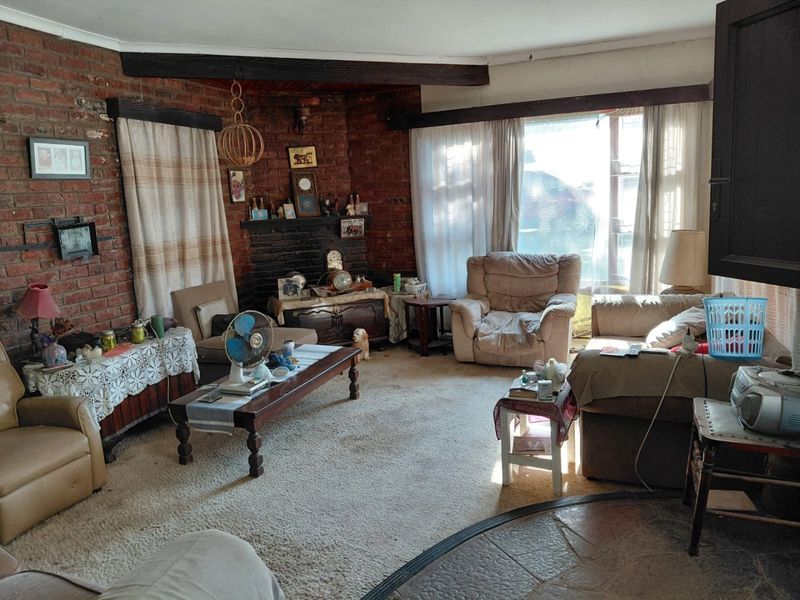 A living room featuring exposed brick walls, a brick fireplace, timber ceiling beams, and stone flooring, offering a rustic aesthetic with potential for modernization.