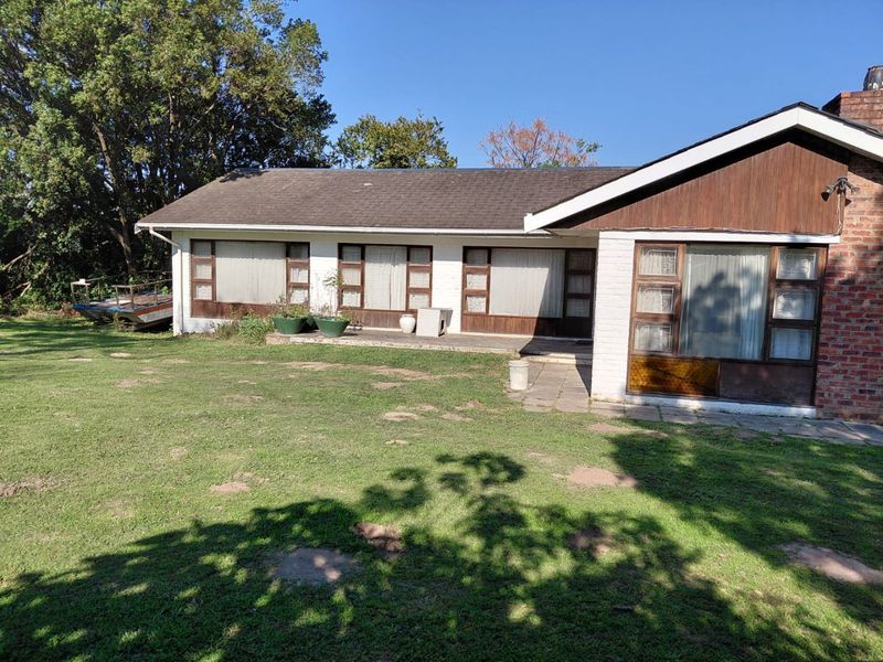 Rear view of a single-story house featuring a brick and timber facade, a paved patio area, and a spacious garden.