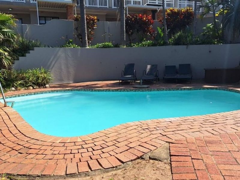 Outdoor swimming pool area featuring brick paving, a retaining wall, and established garden landscaping.