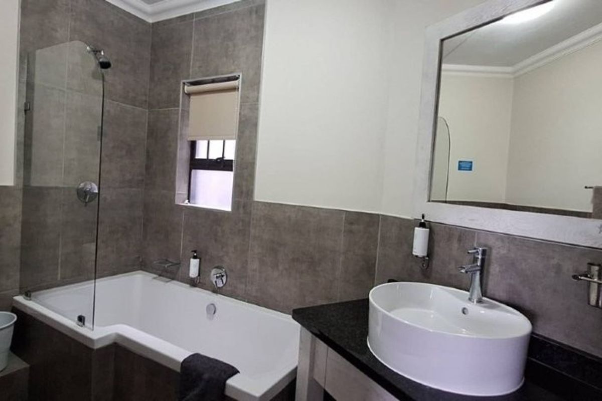 Modern bathroom featuring a bathtub with a glass shower screen, a vanity basin with a granite countertop, and neutral wall tiling.