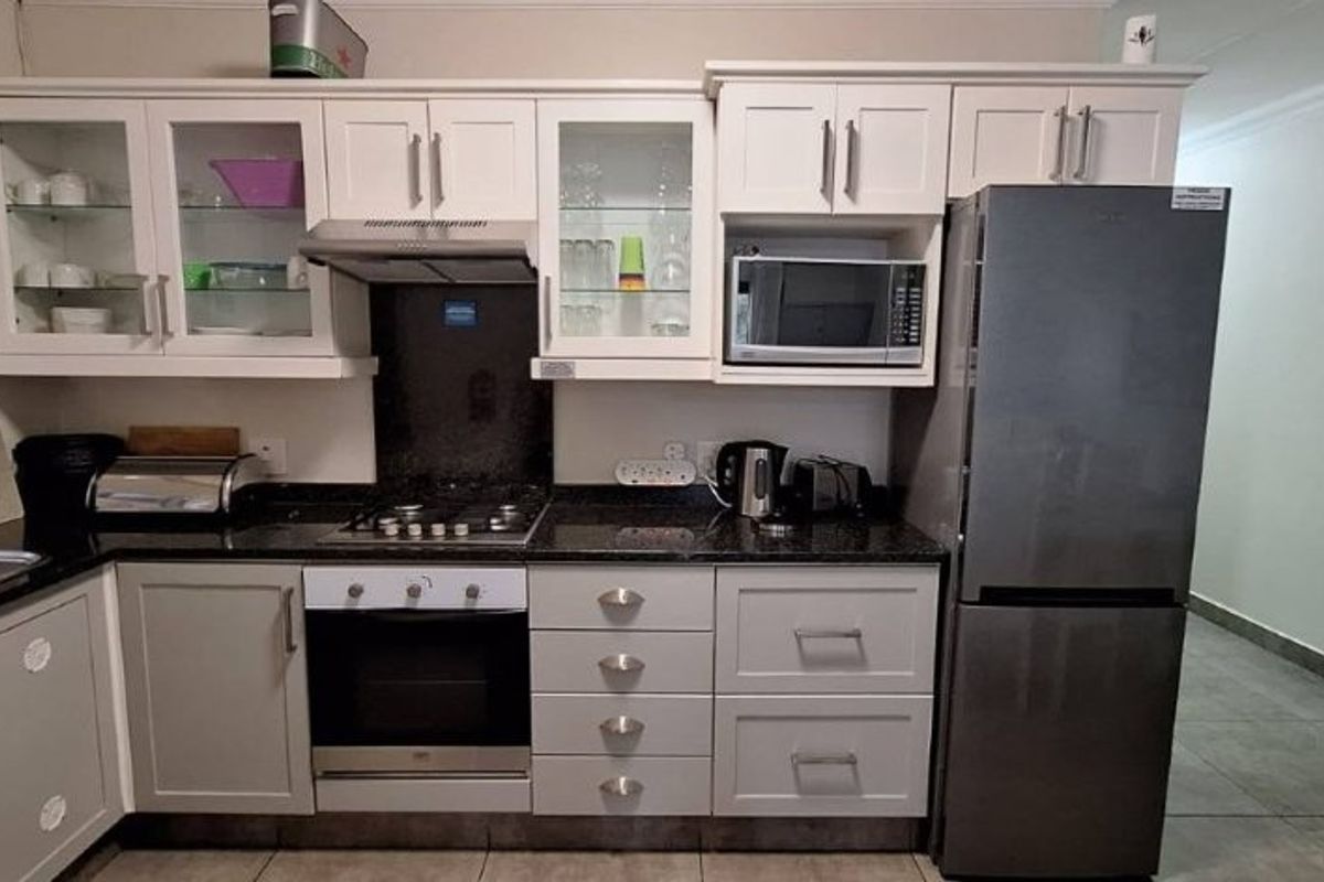 A well-maintained kitchen featuring light-toned cabinetry, granite countertops, integrated appliances including an oven and hob, and durable tiled flooring.