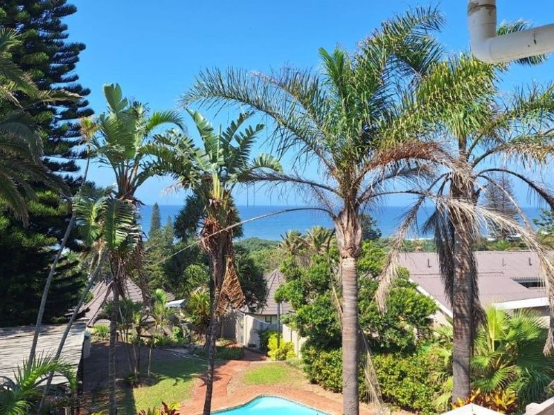A scenic elevated view overlooking a residential complex with a swimming pool, lush tropical landscaping, and a distant ocean horizon.