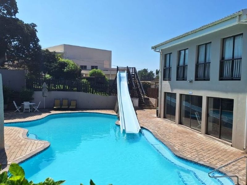 Outdoor pool area featuring a water slide, paved decking, and direct access to the apartment building with balconies and sliding glass doors.