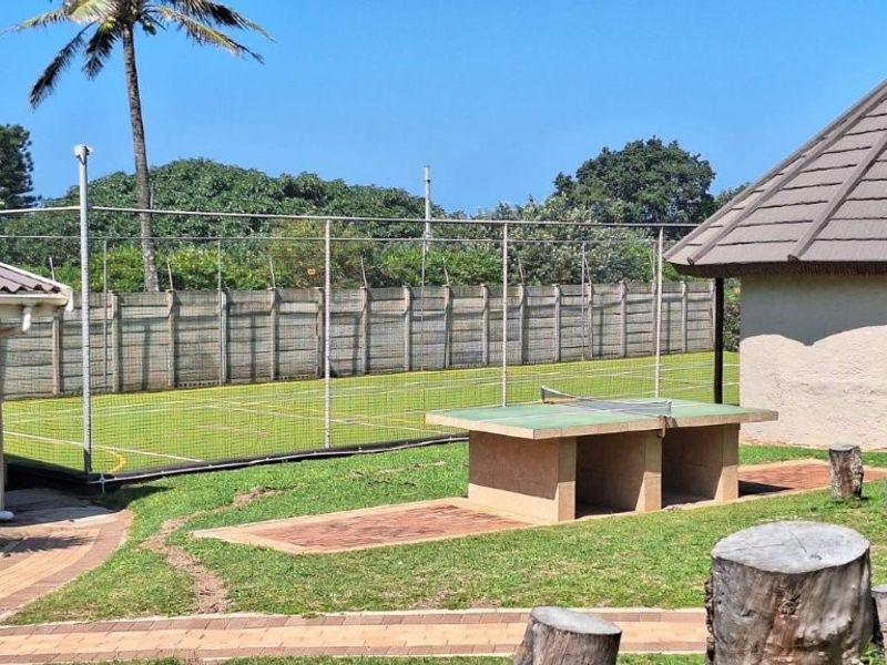 Outdoor recreational area featuring a fenced tennis court and a permanent concrete table tennis table set within a landscaped complex.