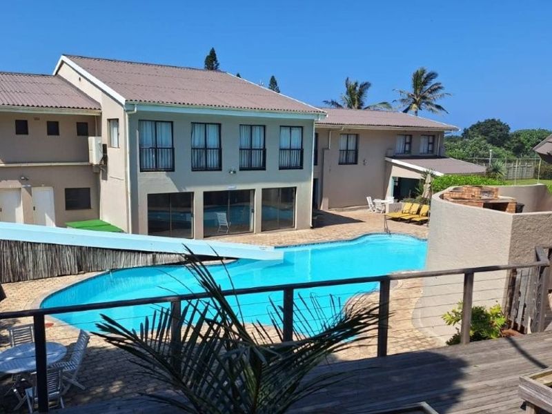 Outdoor pool area featuring a swimming pool with a water slide, built-in braai, and a combination of paved and timber decking.