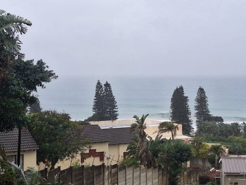 A scenic coastal view overlooking neighboring properties, mature trees, and the ocean horizon under an overcast sky.