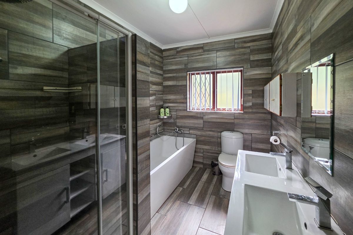 Modern bathroom featuring a double vanity, glass-enclosed shower, built-in bathtub, and contemporary wood-look wall and floor tiling.