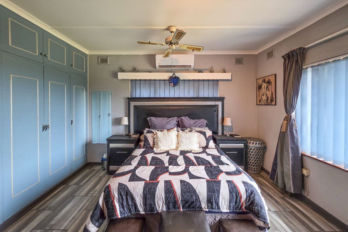 A well-maintained bedroom featuring built-in cupboards, a ceiling fan, and a split-system air conditioner, finished with modern laminate flooring.