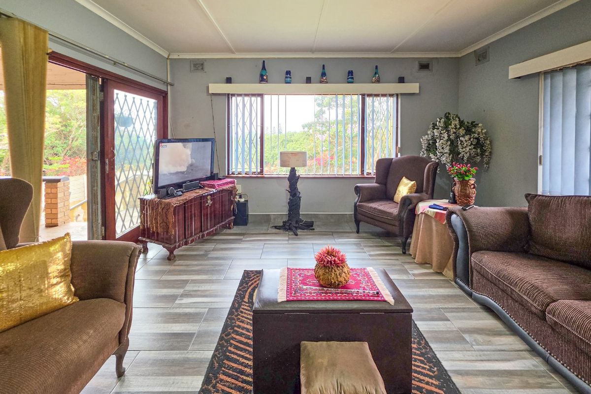 A spacious living room featuring tiled flooring, large windows with security bars, and a sliding glass door providing access to the outdoor area.
