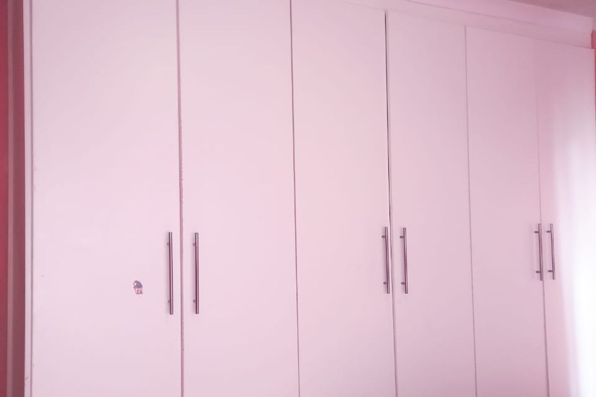 A bedroom featuring a large, white built-in wardrobe with integrated drawers and modern metal handles.