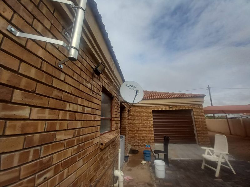 Rear exterior view of the property featuring face brick walls, a satellite dish, security lighting, and a paved patio area leading to the garage.