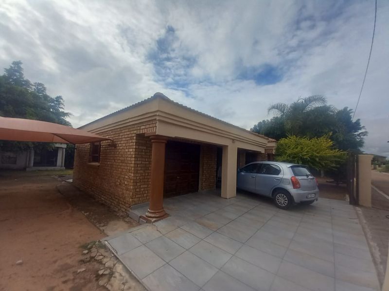 Front exterior view of a face brick house featuring a tiled driveway, garage access, and decorative columns under a cloudy sky.