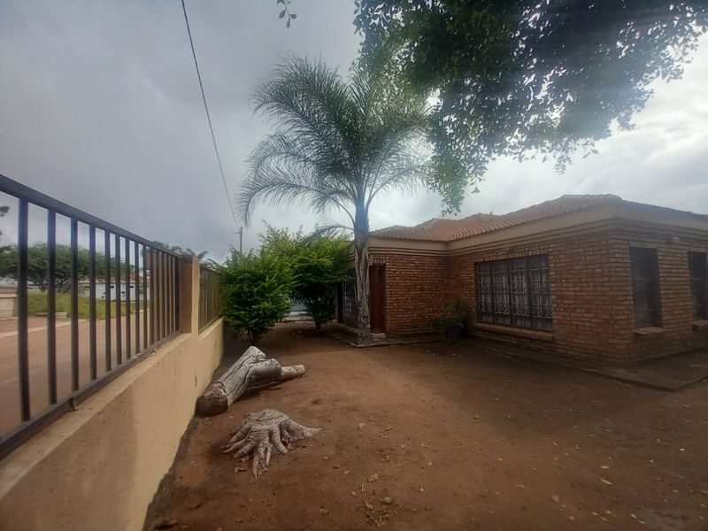 Front exterior view of a face brick house featuring a tiled roof, metal security bars on windows, and a perimeter boundary wall with metal fencing.