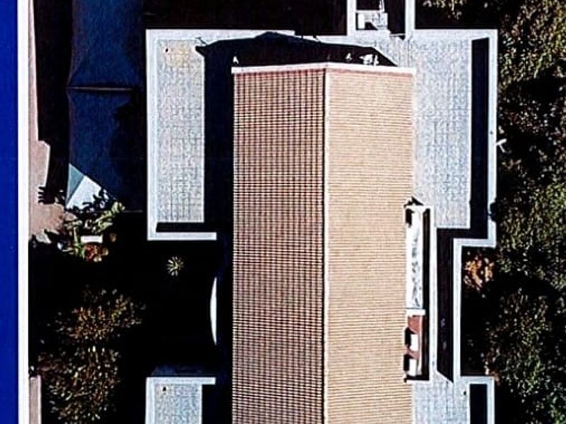Aerial view of the commercial property showing the main building with a tiled roof, surrounding paved areas, and outdoor shade structures.