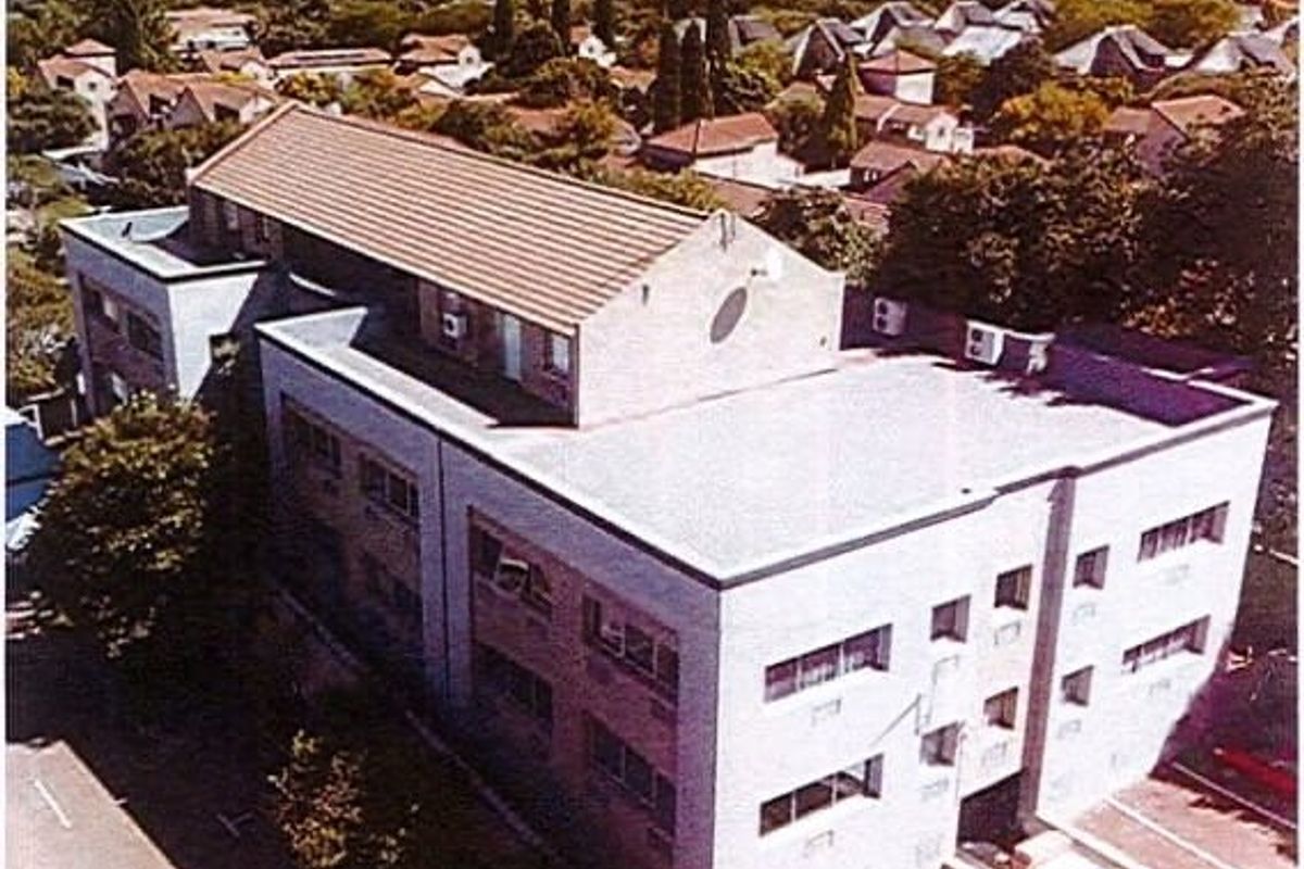 Aerial view of a multi-story commercial building featuring a combination of pitched tiled roofing and flat roof sections with exterior air conditioning units.