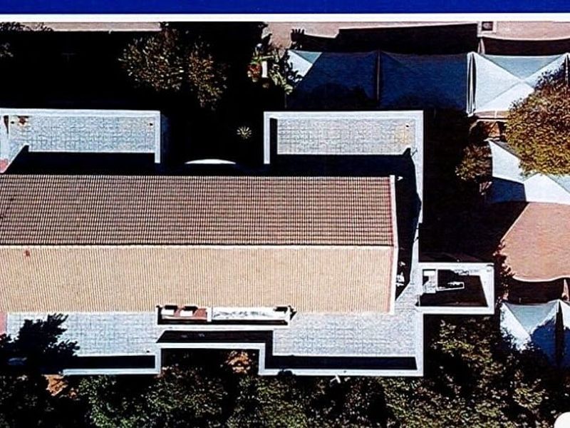 Aerial view of the commercial property showing the main building with a tiled roof, flat roof sections, and a paved parking area with shade sails.