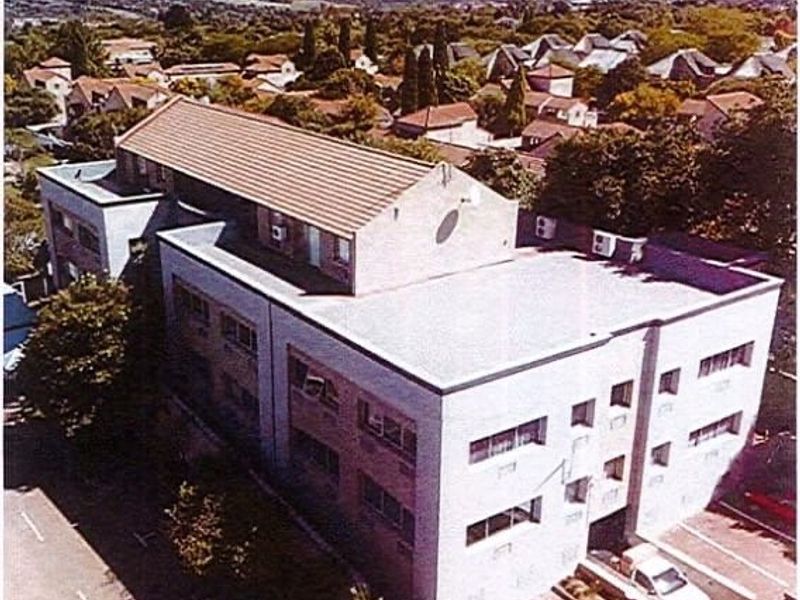 Aerial view of a multi-story commercial building featuring a combination of pitched tiled roofing and flat roof sections with exterior air conditioning units.
