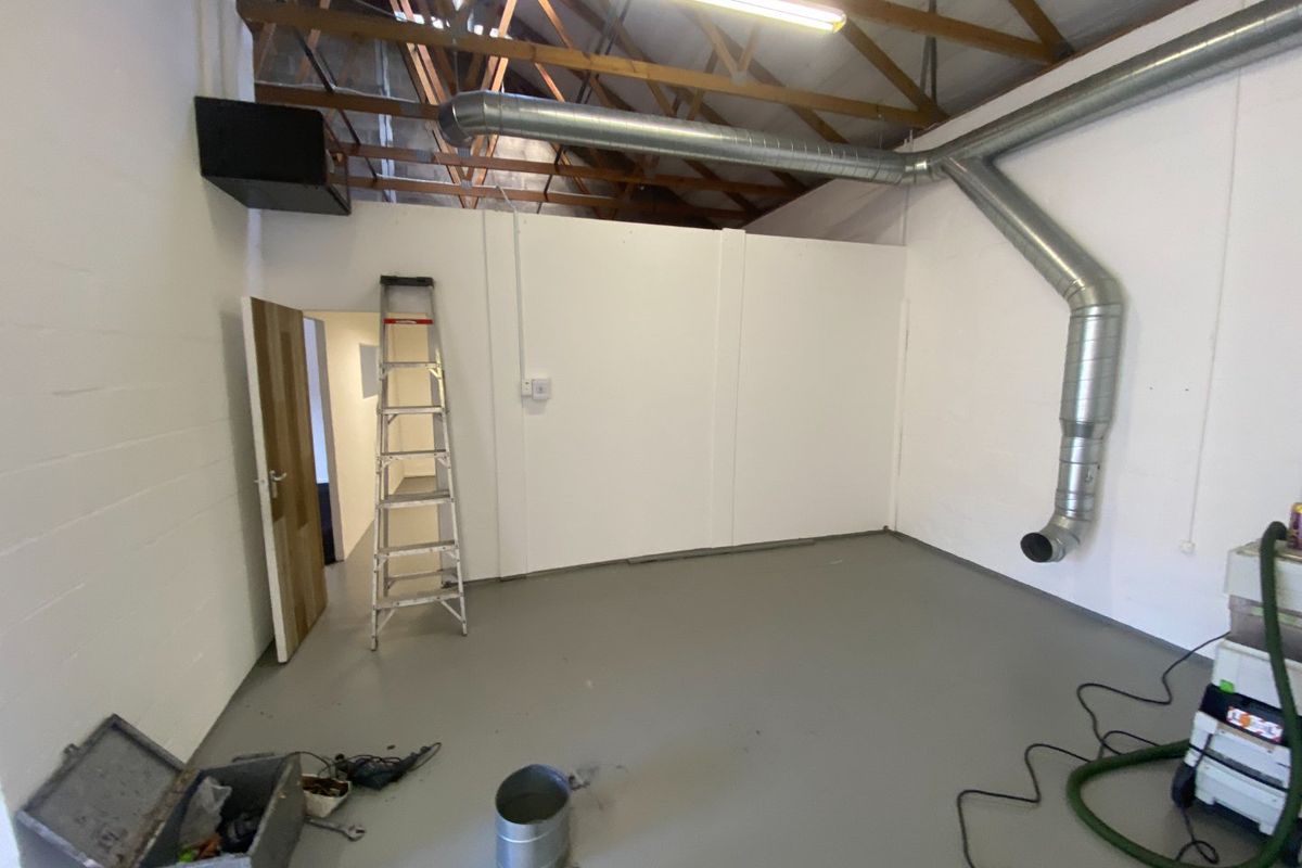 Industrial utility space featuring exposed timber roof trusses, galvanized steel ventilation ducting, and a durable epoxy-coated concrete floor.