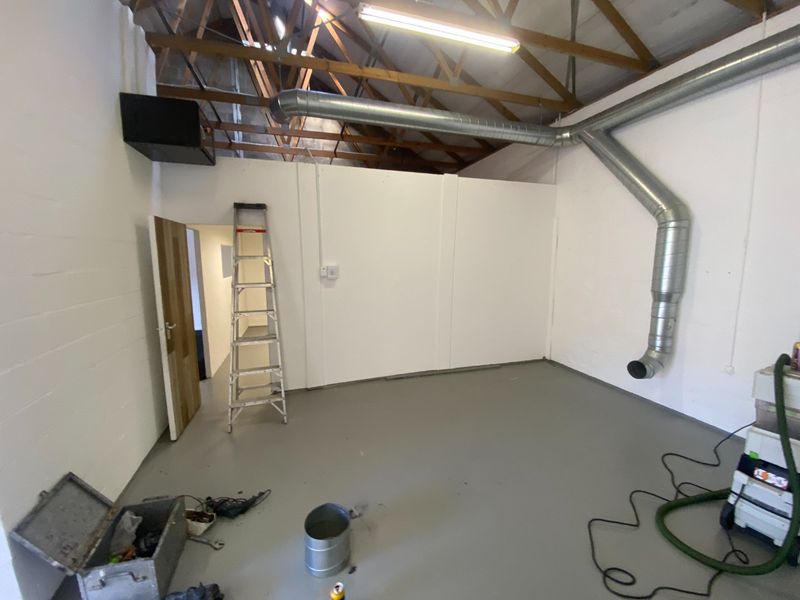 Industrial utility space featuring exposed timber roof trusses, galvanized steel ventilation ducting, and a durable epoxy-coated concrete floor.