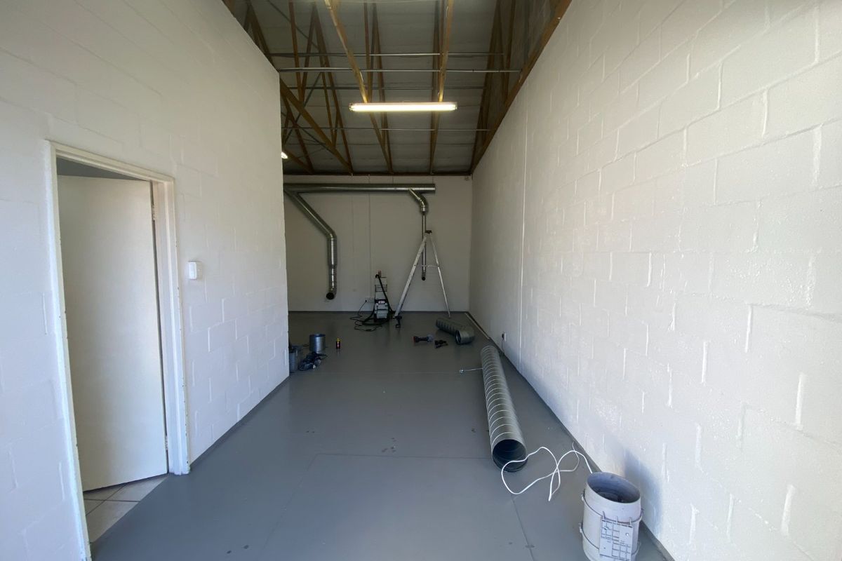 A clean, industrial utility space featuring exposed roof trusses, painted block walls, and durable epoxy flooring, suitable for storage or workshop use.