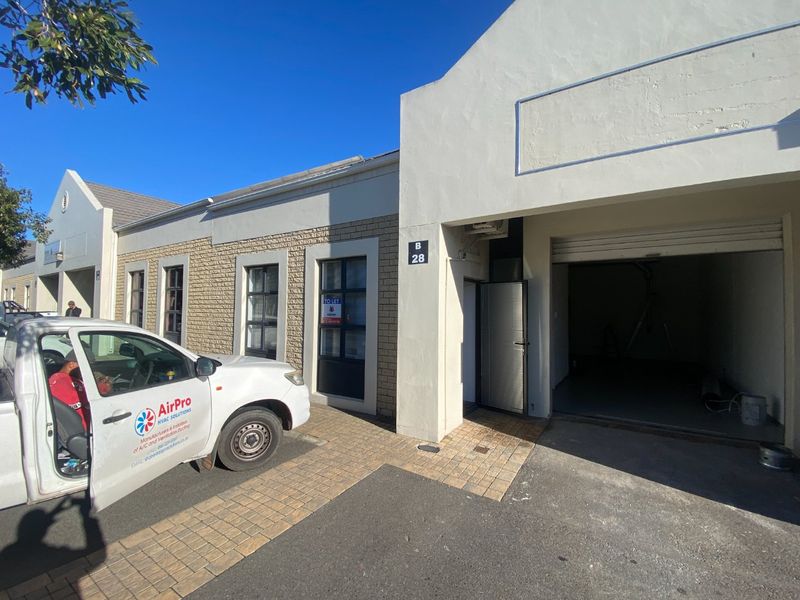 Front elevation of an industrial unit featuring a roller shutter door, brick facade, and paved driveway access.