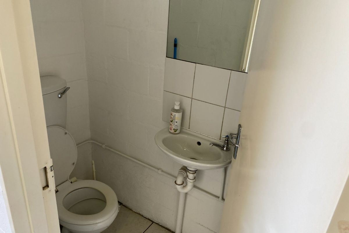 A compact industrial-style bathroom featuring a wall-mounted basin, tiled splashback, and standard toilet with exposed plumbing.