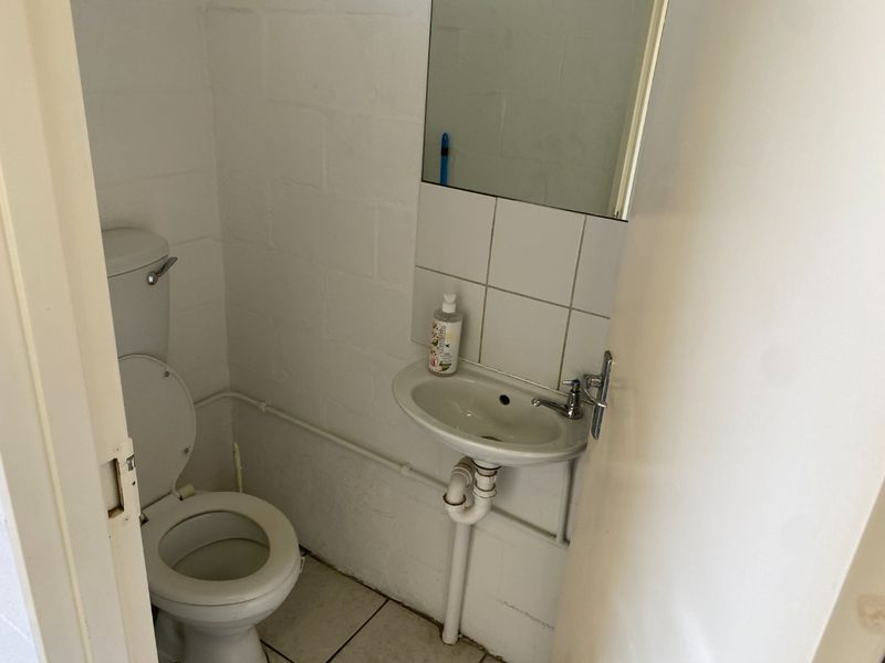 A compact industrial-style bathroom featuring a wall-mounted basin, tiled splashback, and standard toilet with exposed plumbing.