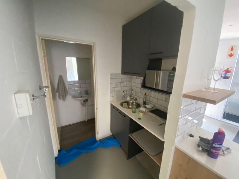 Compact scullery area featuring dark cabinetry, subway tile backsplash, and a stainless steel sink, with an adjacent small bathroom area.
