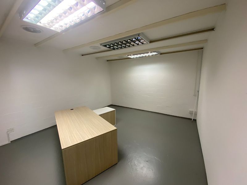 A clean, minimalist office space featuring painted brick walls, durable epoxy flooring, and overhead fluorescent lighting, suitable for a professional work environment.