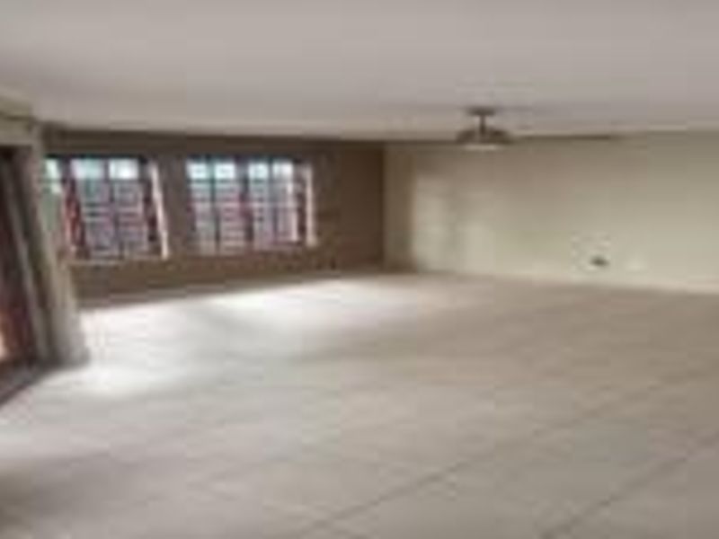 A spacious, empty living room featuring neutral tiled flooring, a ceiling fan, and access to the outdoors through classic french doors.
