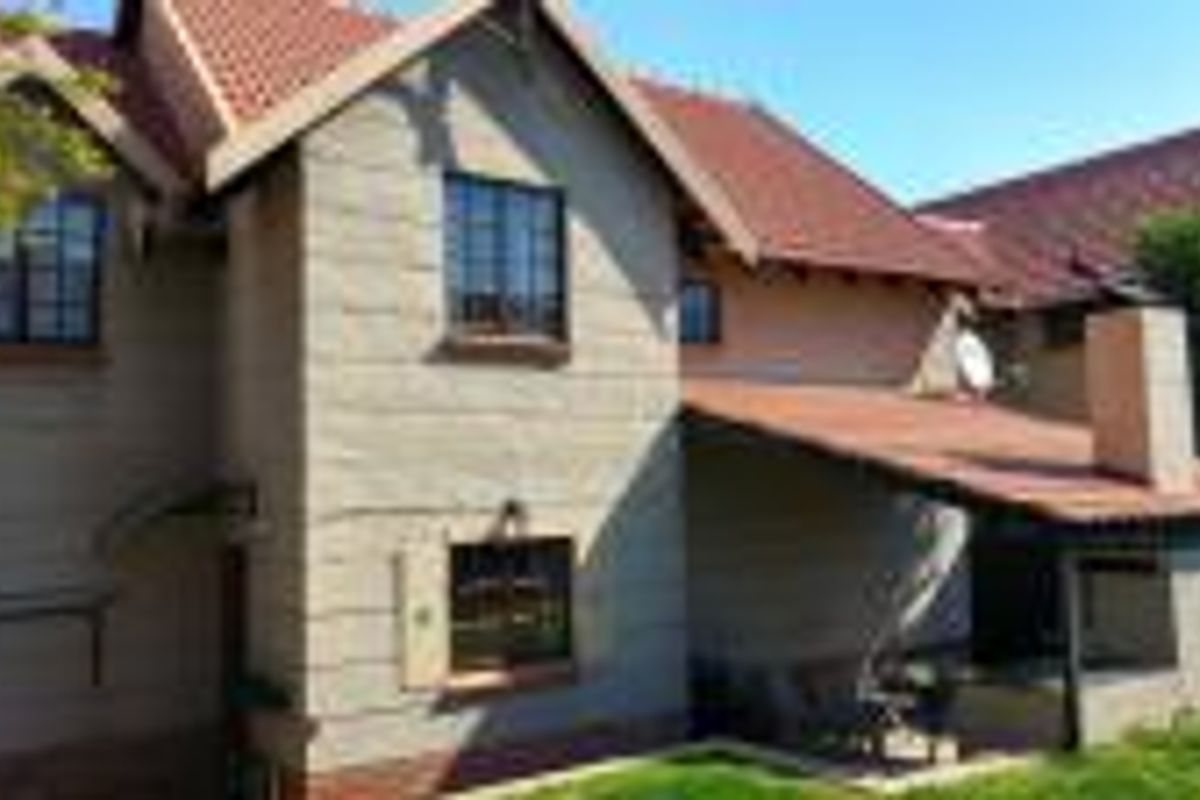 Rear view of the townhouse featuring a tiled roof, a covered patio area with a built-in braai, and a small garden space.