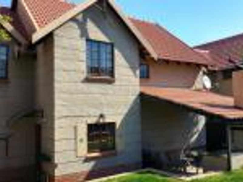 Rear view of the townhouse featuring a tiled roof, a covered patio area with a built-in braai, and a small garden space.