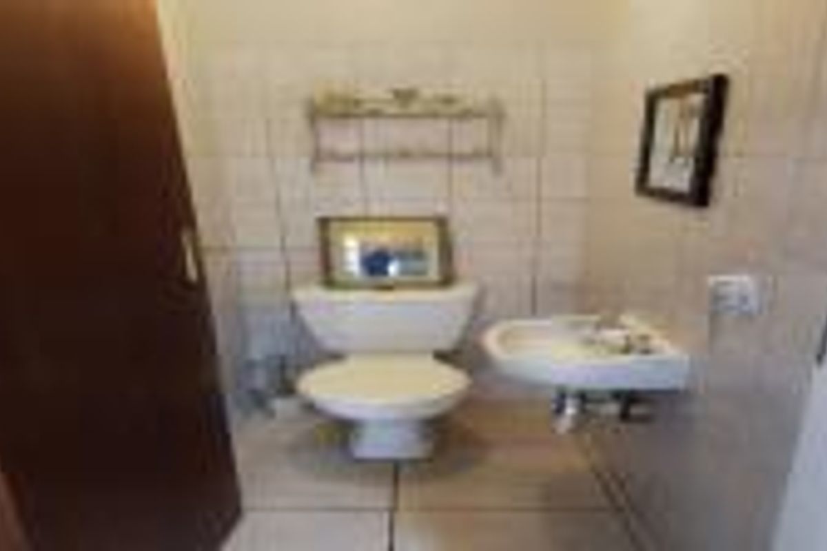 A compact guest bathroom featuring a standard toilet and a wall-mounted basin with neutral ceramic wall and floor tiling.