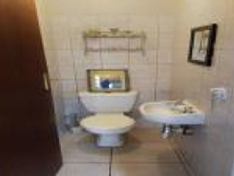 A compact guest bathroom featuring a standard toilet and a wall-mounted basin with neutral ceramic wall and floor tiling.