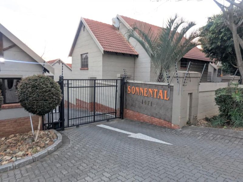 Front entrance view of the Sonnental townhouse complex featuring a secure gated access point, paved driveway, and perimeter electric fencing.