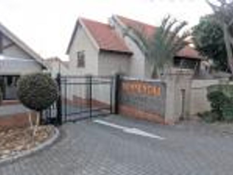 Front entrance view of the townhouse complex featuring a paved driveway, secure wrought iron gate, and brick boundary wall.