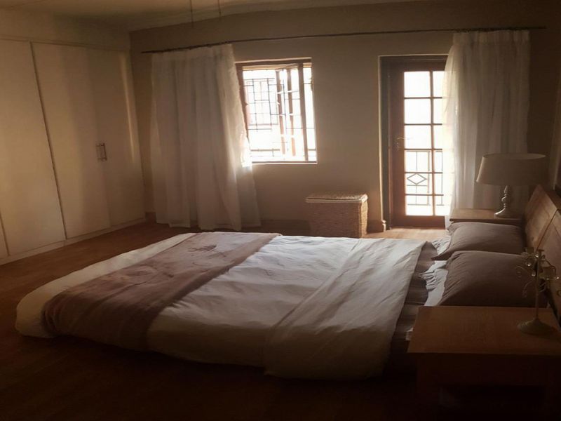 A bedroom featuring built-in cupboards, laminate flooring, and direct access to an outdoor area through a glass panel door.